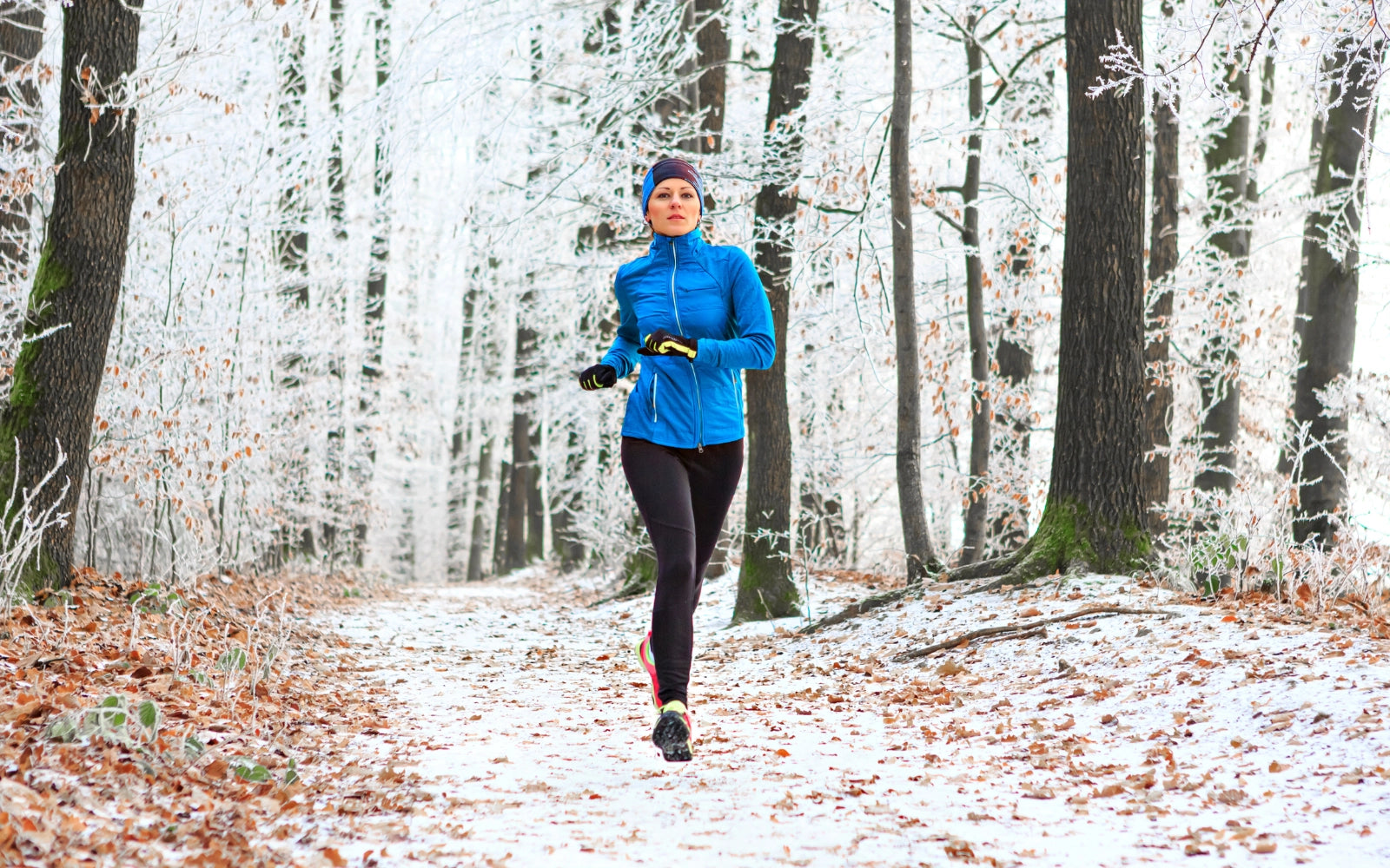 Kobieta biegnąca przez ośnieżony las w zimie